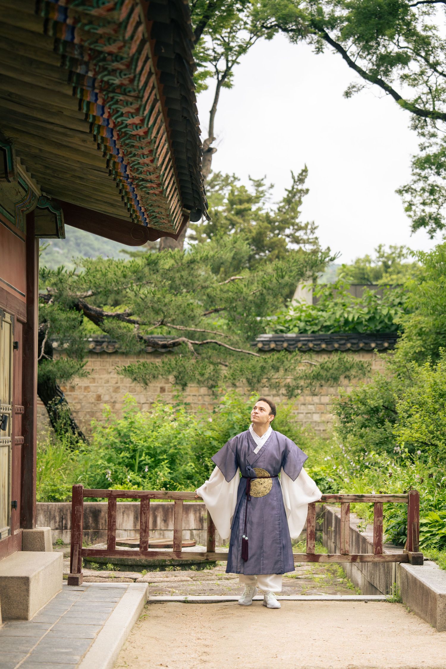 A person in traditional Korean hanbok clothing walks along a wooden veranda at a historic temple or palace complex.