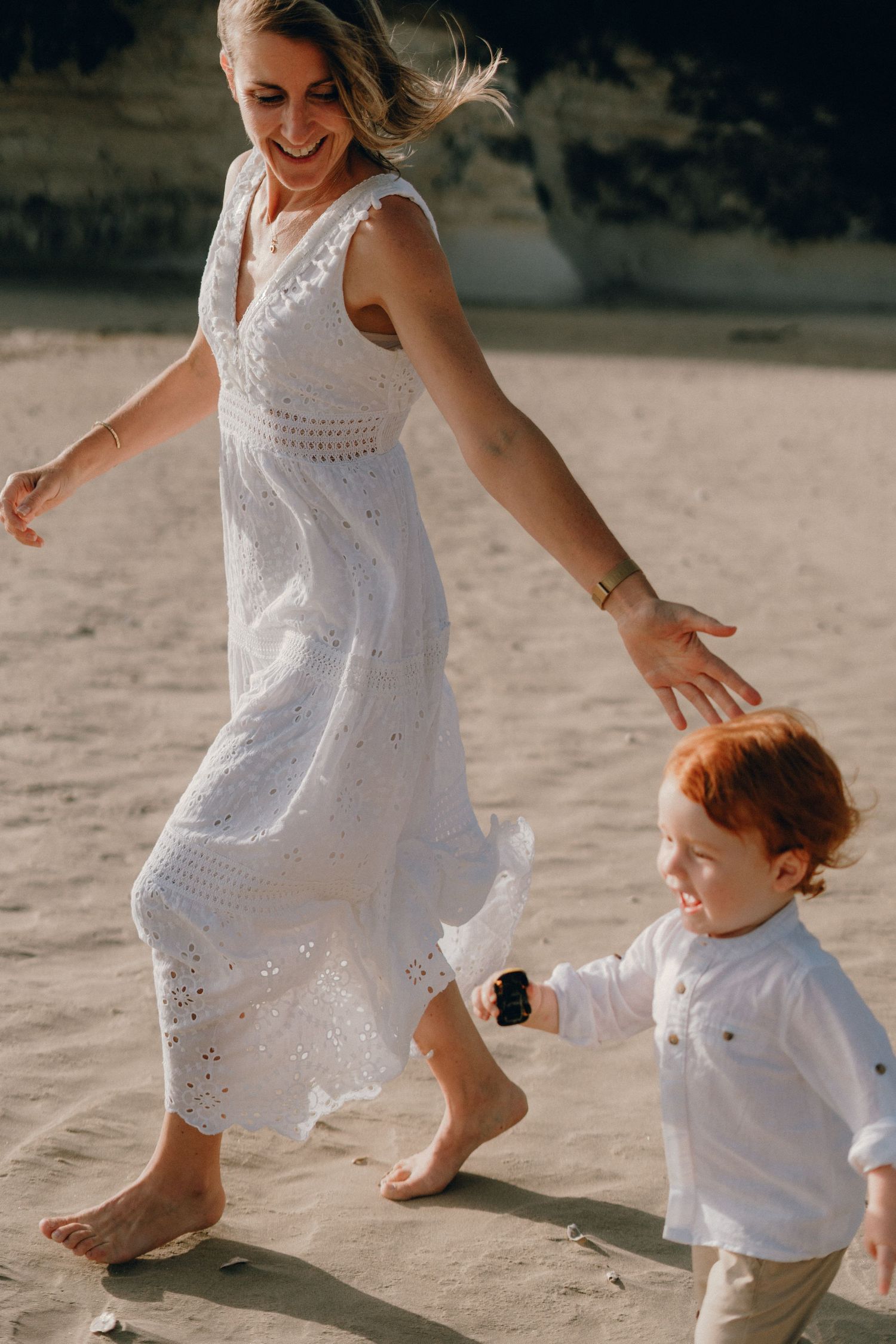 Une mère et son fils courant sur la plage, heureux, cheveux au vent.