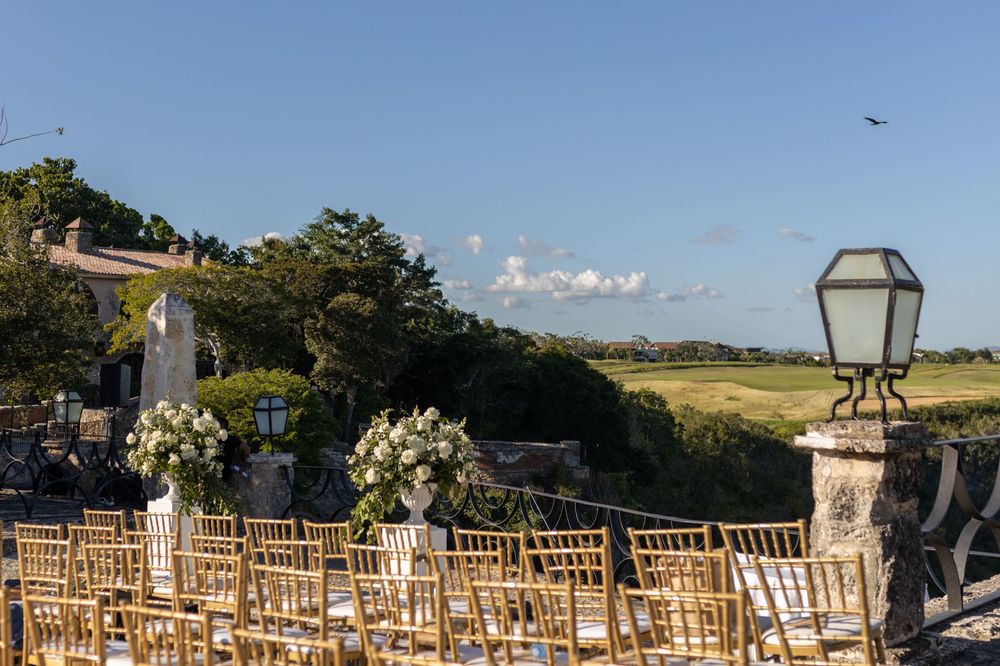 Outdoor wedding ceremony setup with gold chairs and floral arrangements overlooking a golf course.