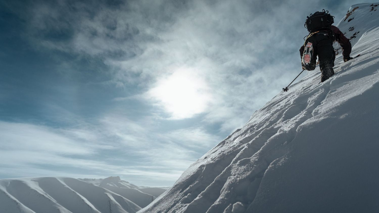 Skiers and snowboarders descend a snowy mountain slope under dramatic cloudy skies.