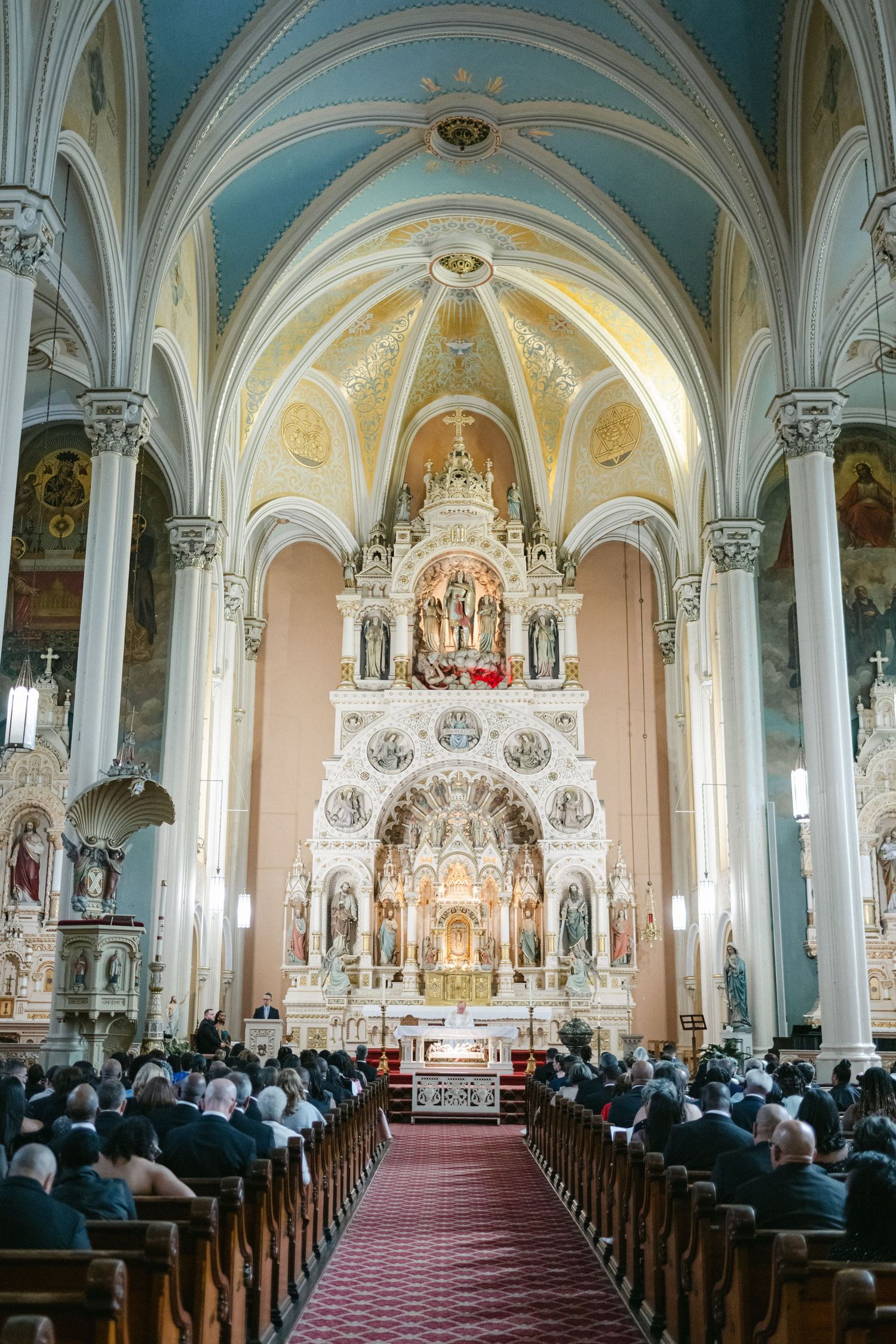 Interior view of a Gothic revival church with ornate altar, vaulted ceilings, and congregation seated in wooden pews.