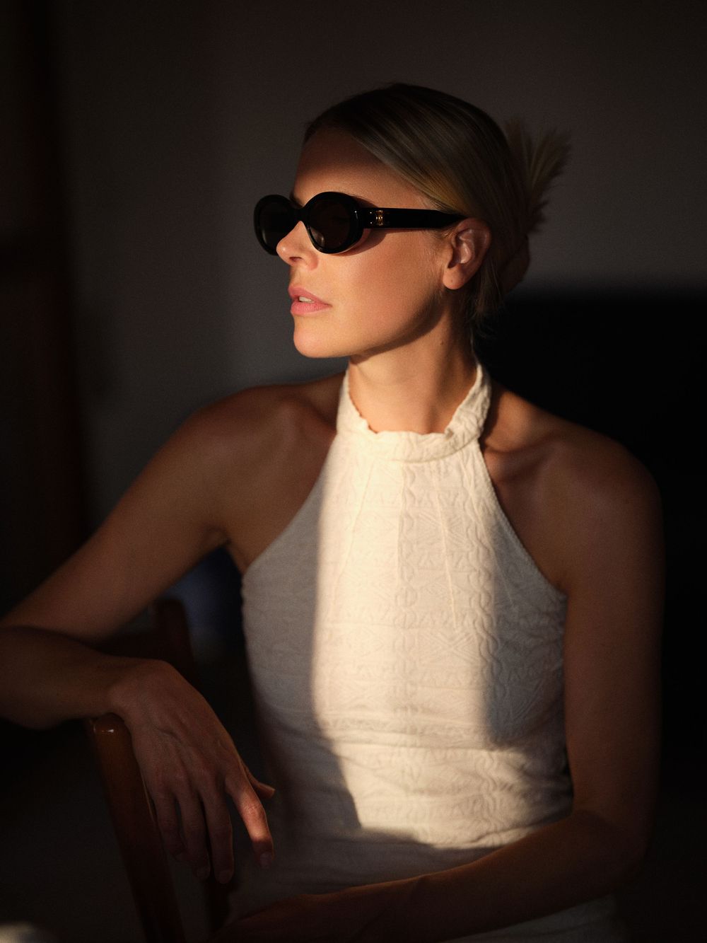 A dramatic fashion portrait series in black and white showing a figure in a white sleeveless top against dark shadows.