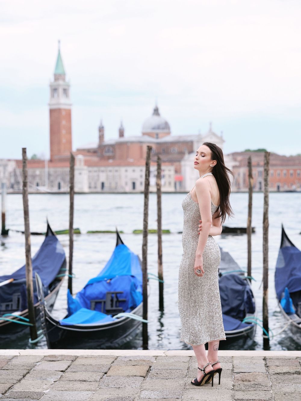 Woman in white dress poses along Venice canal with gondolas and San Giorgio Maggiore church in background.