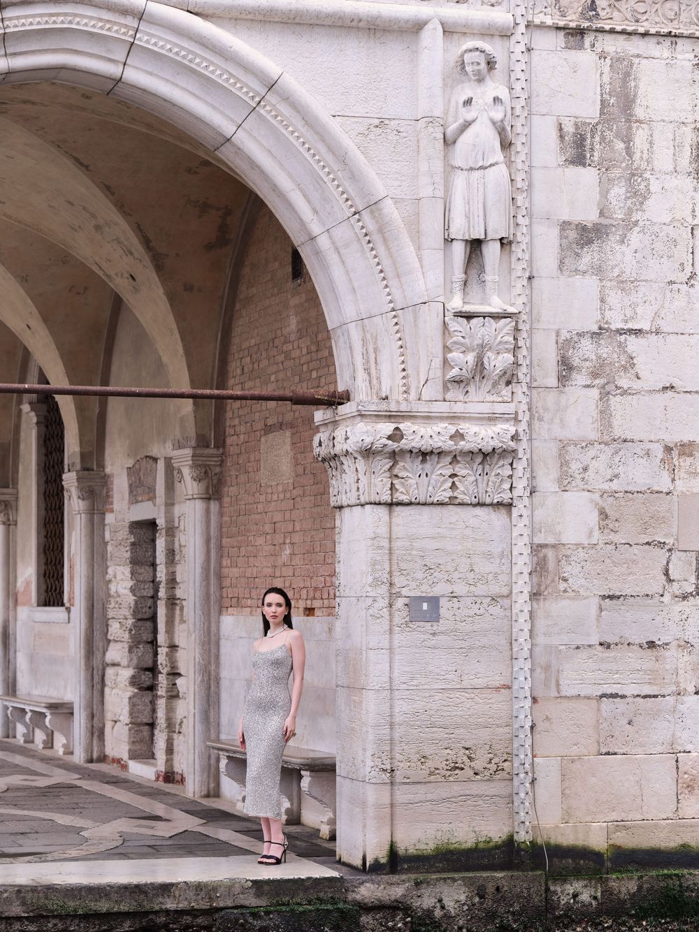 A series of white stone arches with ornate architectural details line a covered walkway in an ancient European building.