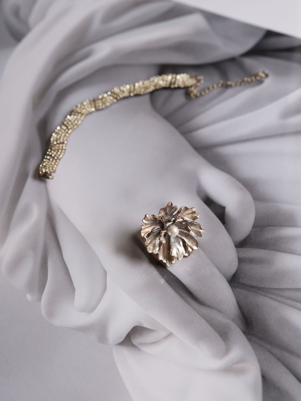 Delicate jewelry pieces including silver leaf designs and chains displayed on soft gray fabric in an artistic arrangement.