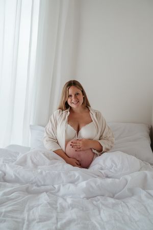 Zwangerschapsfotoshoto blote buik lingerie in bed in daglicht studio M te Moerbeke. Melissa Stuer Moederschapsfotograaf  fotograaf