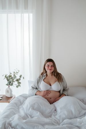 Zwangerschapsfotoshoot met blote buik en lingerie in  bed van daglicht studio M te Moerbeke. Melissa Stuer Moederschapsfotograaf  fotograaf