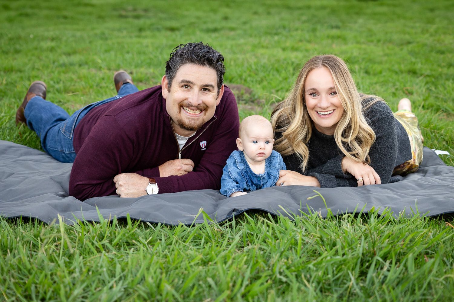 A family lies together on lush green grass during an outdoor photo session near San Jose