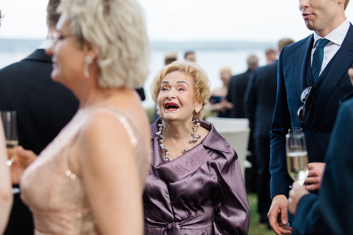 A group of well-dressed wedding guests socialize and laugh during an elegant reception event.