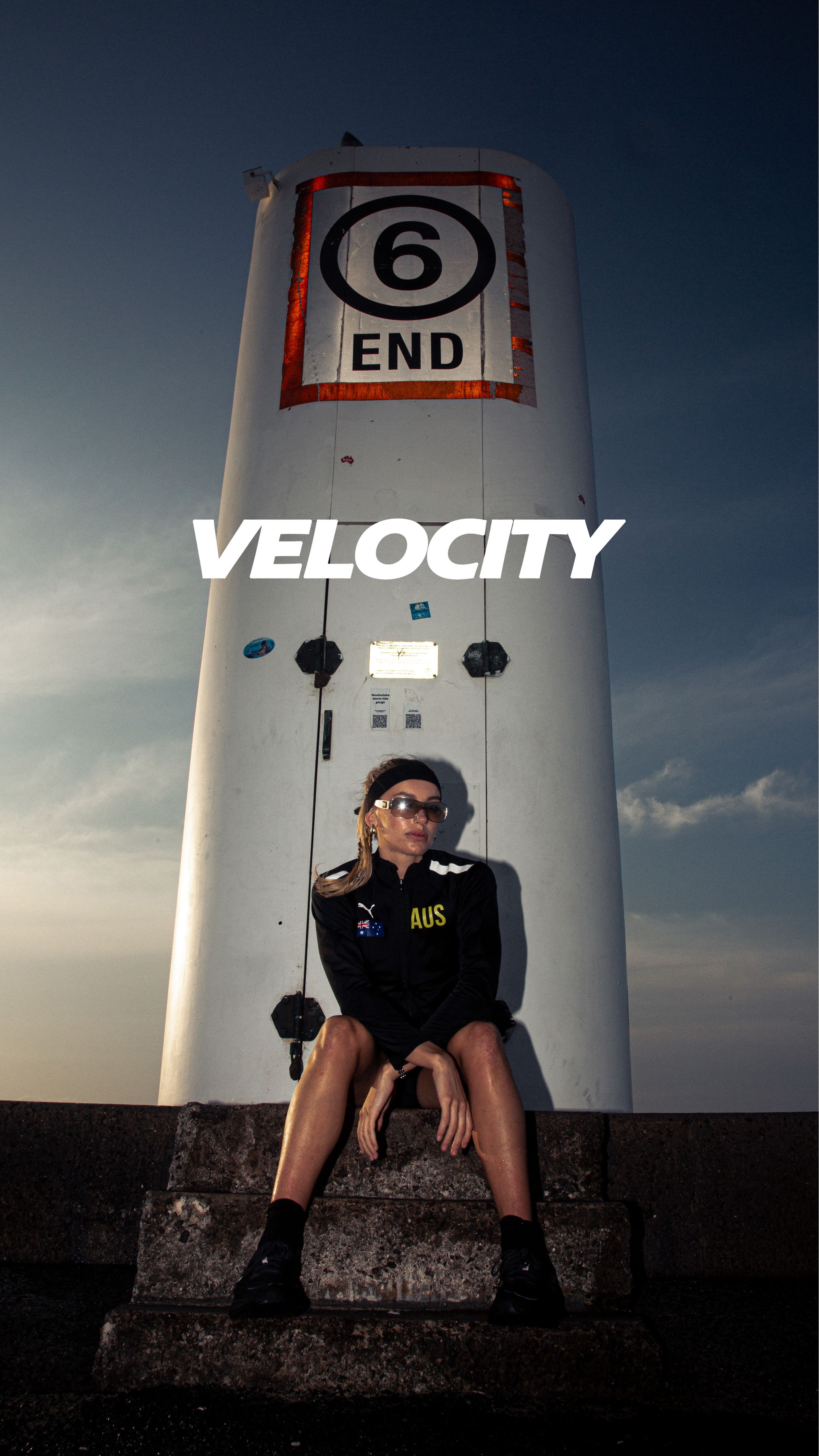 A person sits at the base of a white lighthouse with a number 6 end sign against a dramatic cloudy sky.