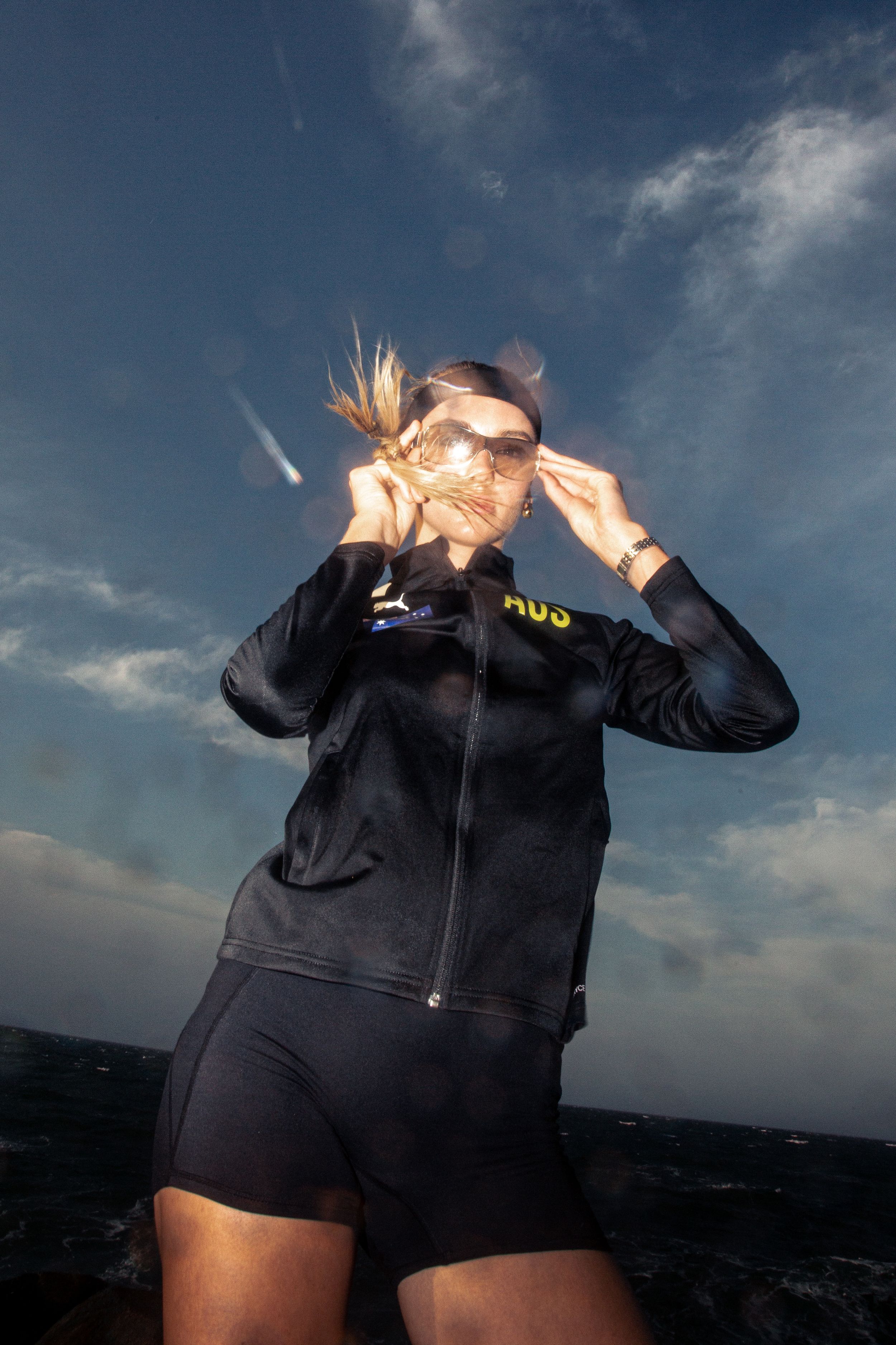 A person in black athletic wear stands against a dramatic cloudy sky at sunset.