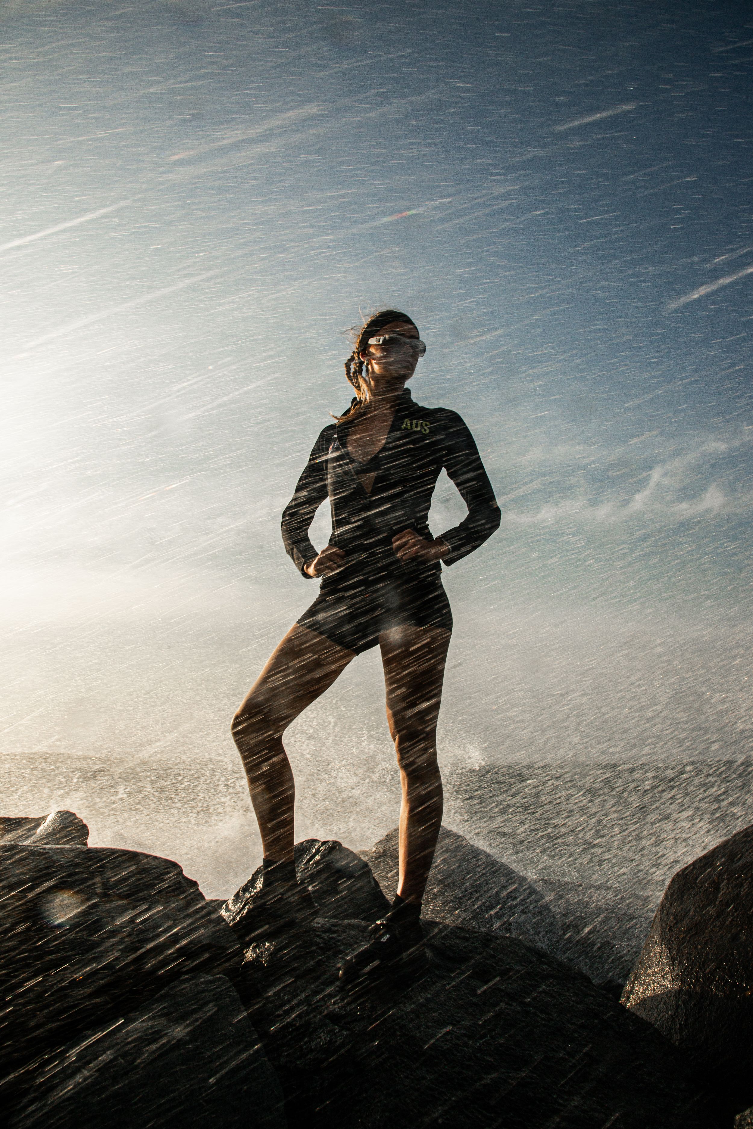 Silhouetted figure stands dramatically on rocky outcrop against stormy sky at sunset.