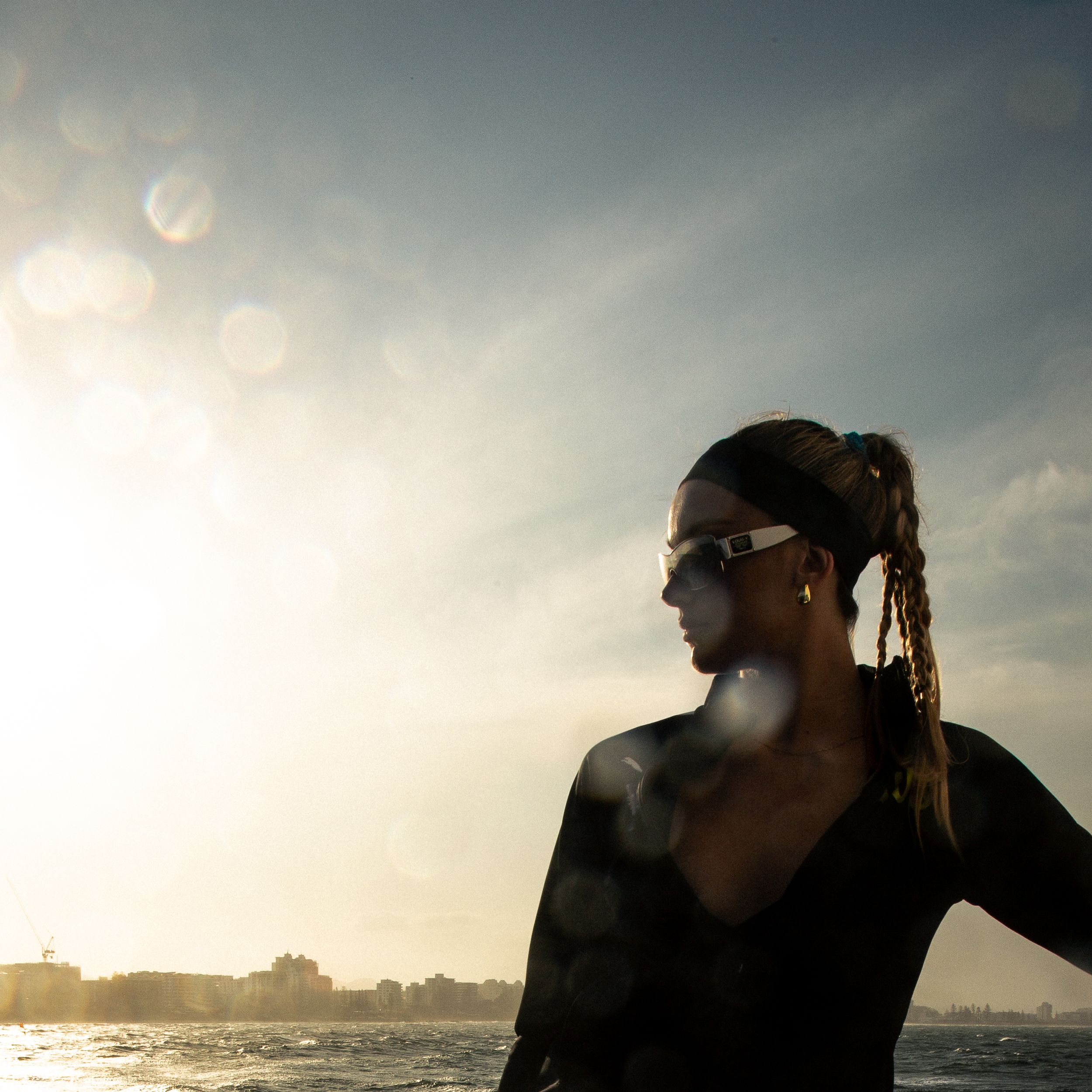 A silhouetted figure with sunglasses gazes at the ocean horizon during a moody sunset with dramatic clouds.