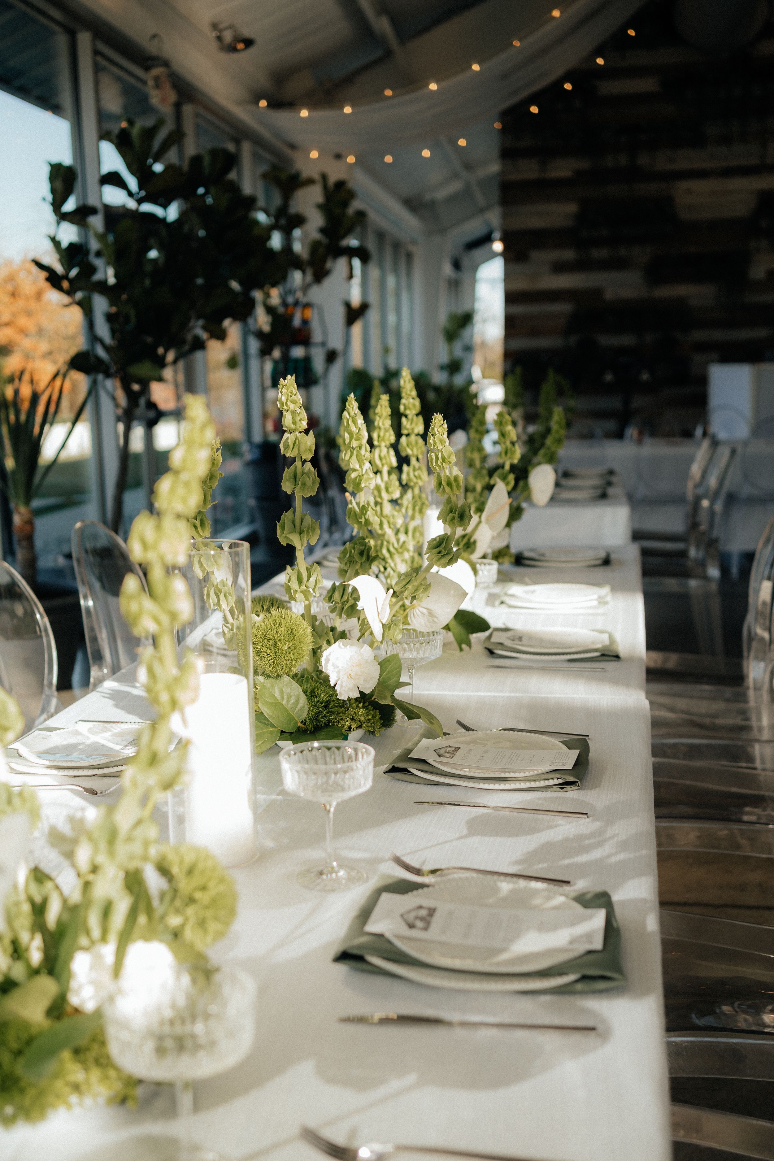 Elegant white table settings with delicate floral centerpieces and string lights create a romantic wedding reception atmosphere.