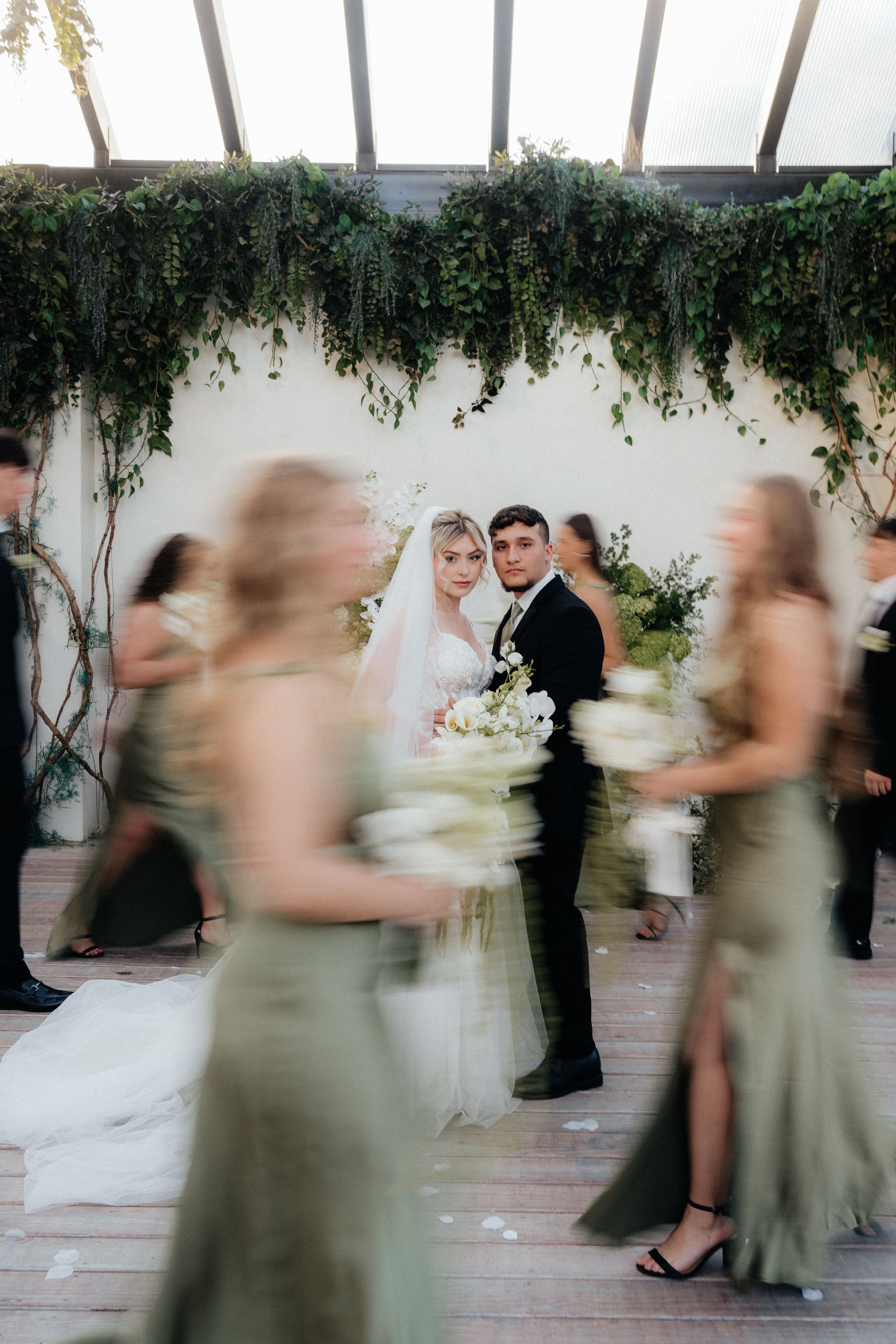 Motion blur captures wedding party dancing in a sequence of candid moments under hanging greenery at an elegant reception.