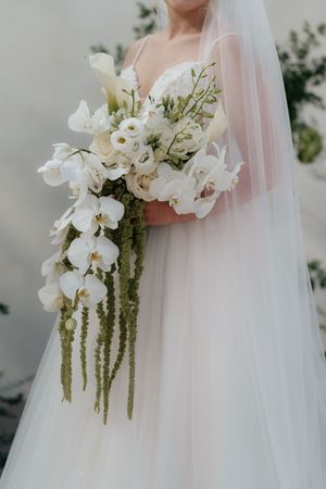 Close-up details of an elegant white orchid and cascading amaranthus wedding bouquet with flowing tulle veil.