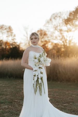 Elegant white wedding gown and bouquet of white flowers captured in golden sunset light outdoors.