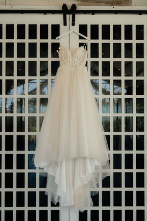White tulle wedding dresses hanging in a row against a lattice wall backdrop.