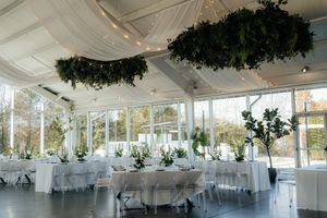 Elegant white wedding reception venue with hanging greenery and string lights under a draped ceiling.