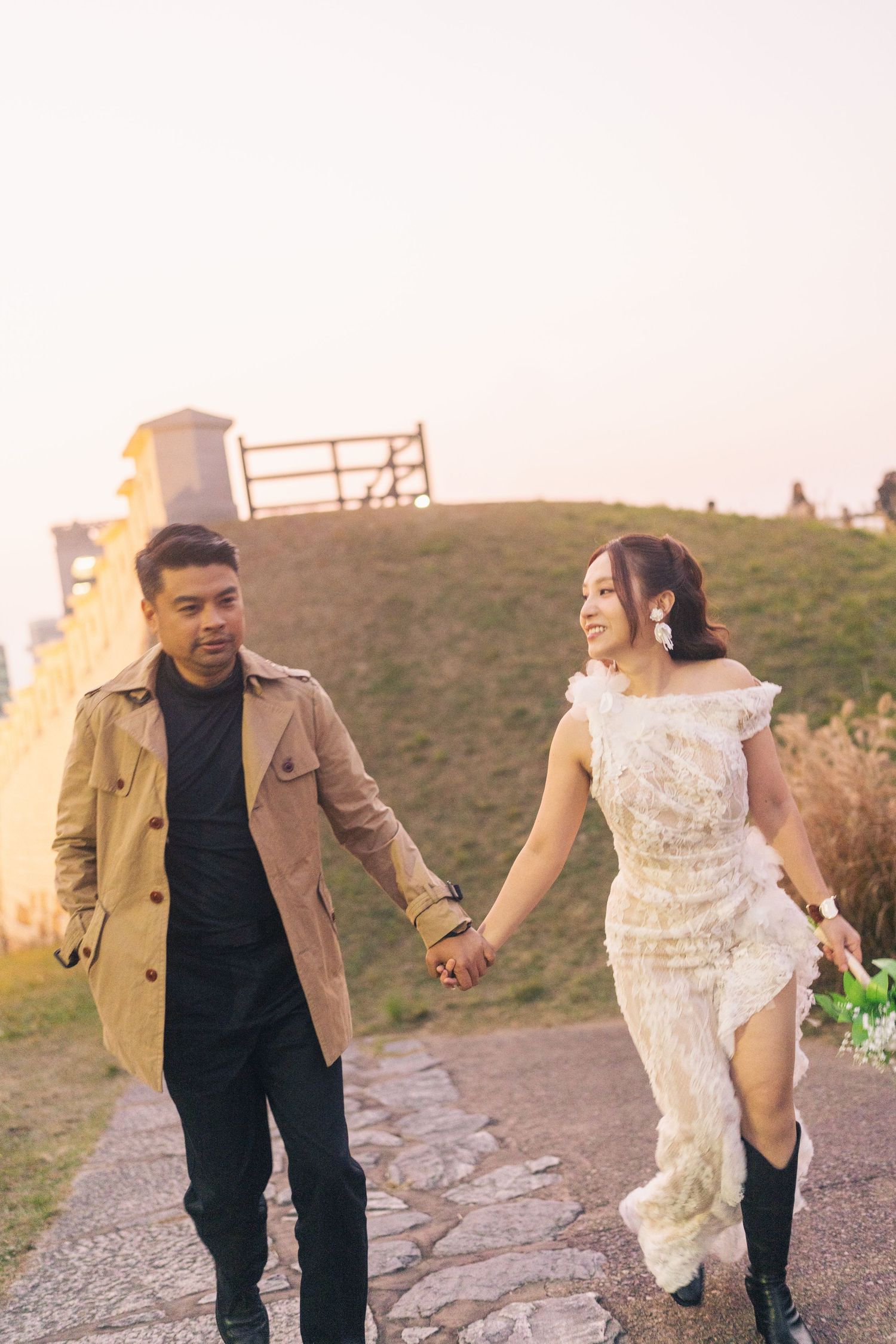 A couple walks along a stone path at sunset during a romantic outdoor photoshoot.
