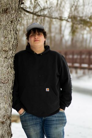 Person in dark winter clothing standing between bare trees in snowy landscape.