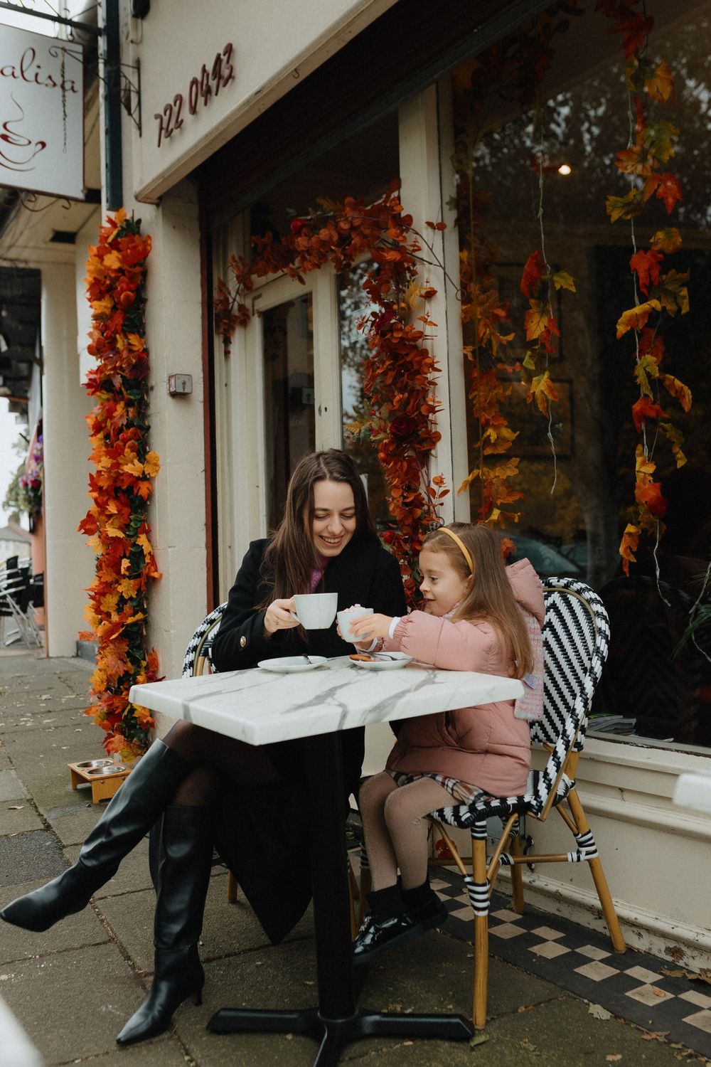 A cozy cafe scene with autumn decorations featuring orange leaves framing the storefront and outdoor seating.