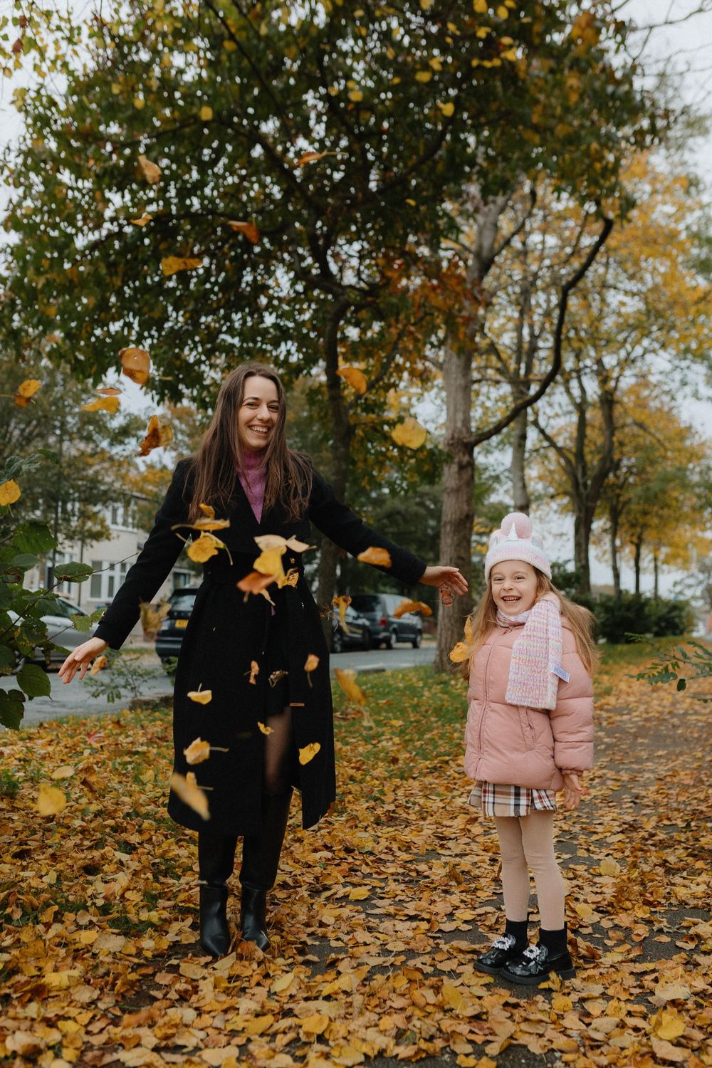 Two people enjoying a fall day together on a leaf-covered path with golden autumn foliage falling around them.