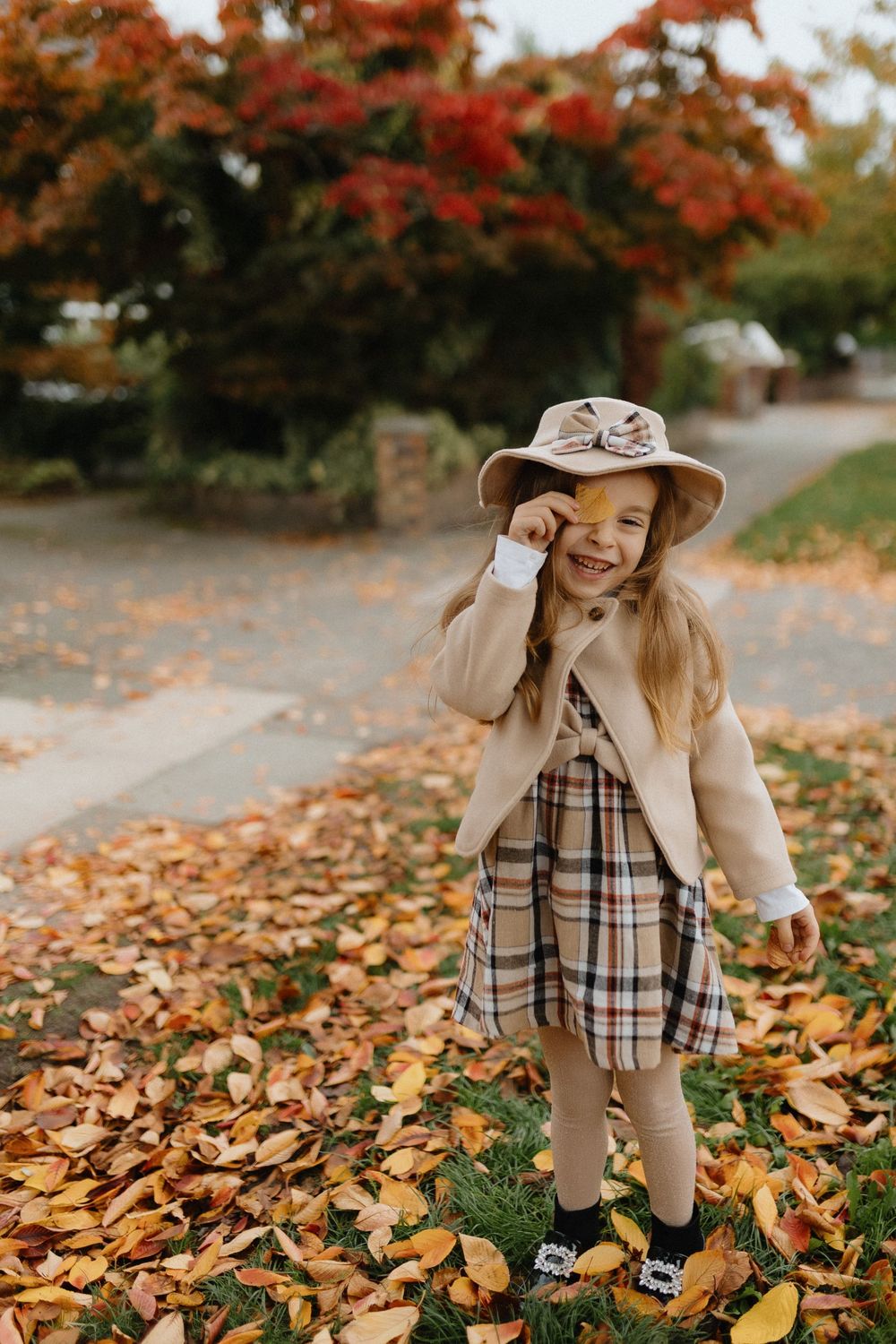 A series of fall photos showing a child in a beige coat and plaid dress playing in autumn leaves under red maple trees.