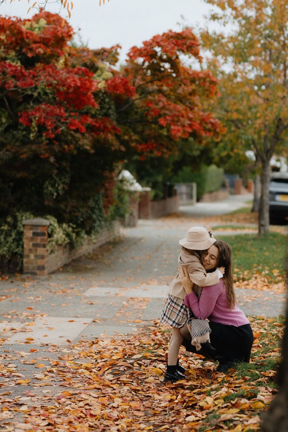 Two friends sit together on fallen autumn leaves beneath vibrant red maple trees on a peaceful path.