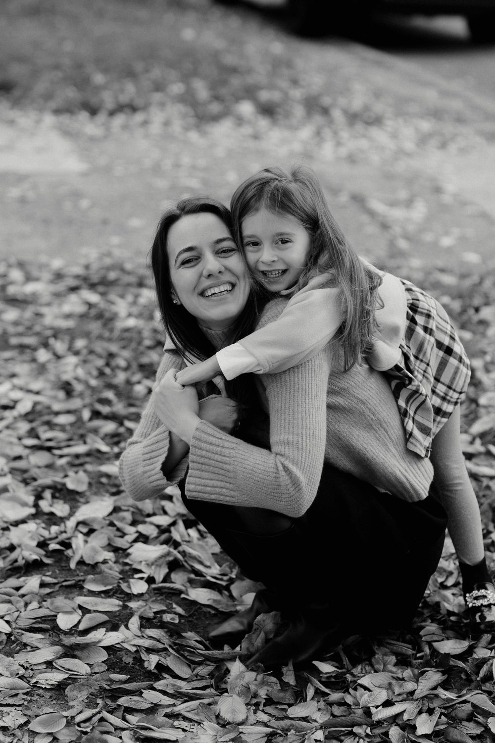 Black and white photo series showing joyful moments between two people playing in fallen autumn leaves.