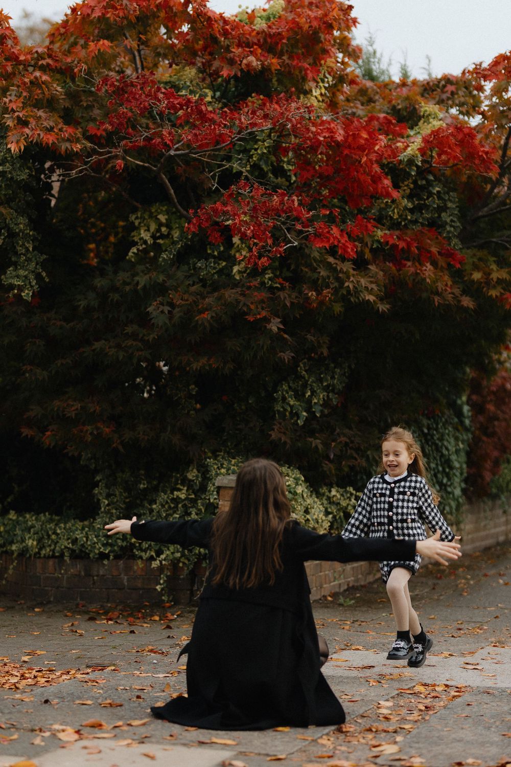 Two people share a joyful moment beneath vibrant red autumn foliage on a path covered with fallen leaves.