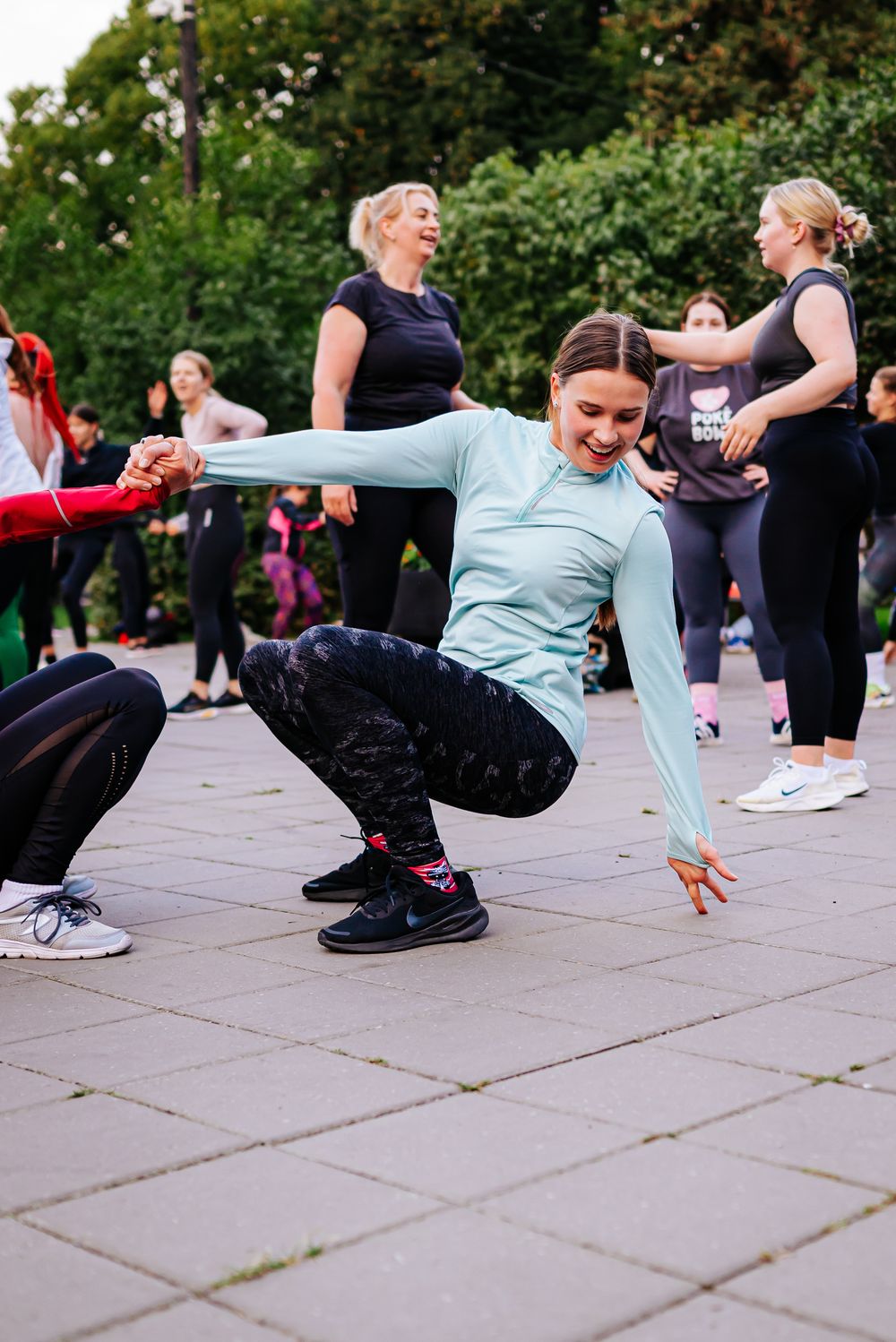 A group of people performing dynamic stretching exercises during an outdoor fitness class on paved ground.