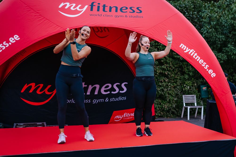 People exercising outdoors under red fitness branded inflatable arches during a community fitness event.