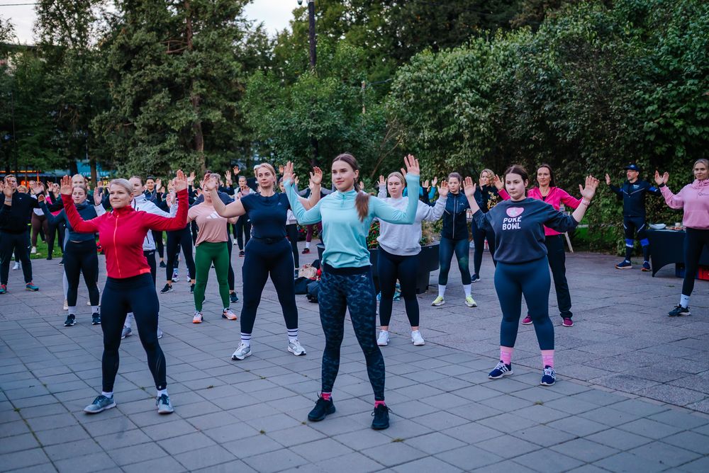 Large group of people exercising together outdoors in a park during a fitness class session.