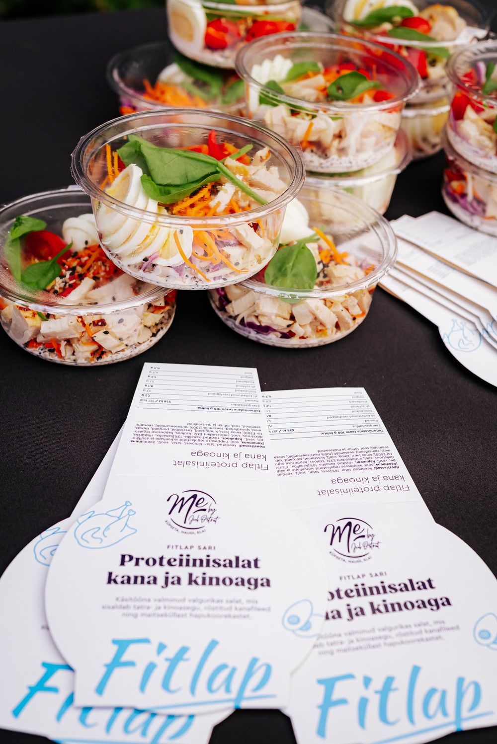 Fresh protein salads in clear plastic containers with quinoa and vegetables displayed next to Fitlap branded menu cards.
