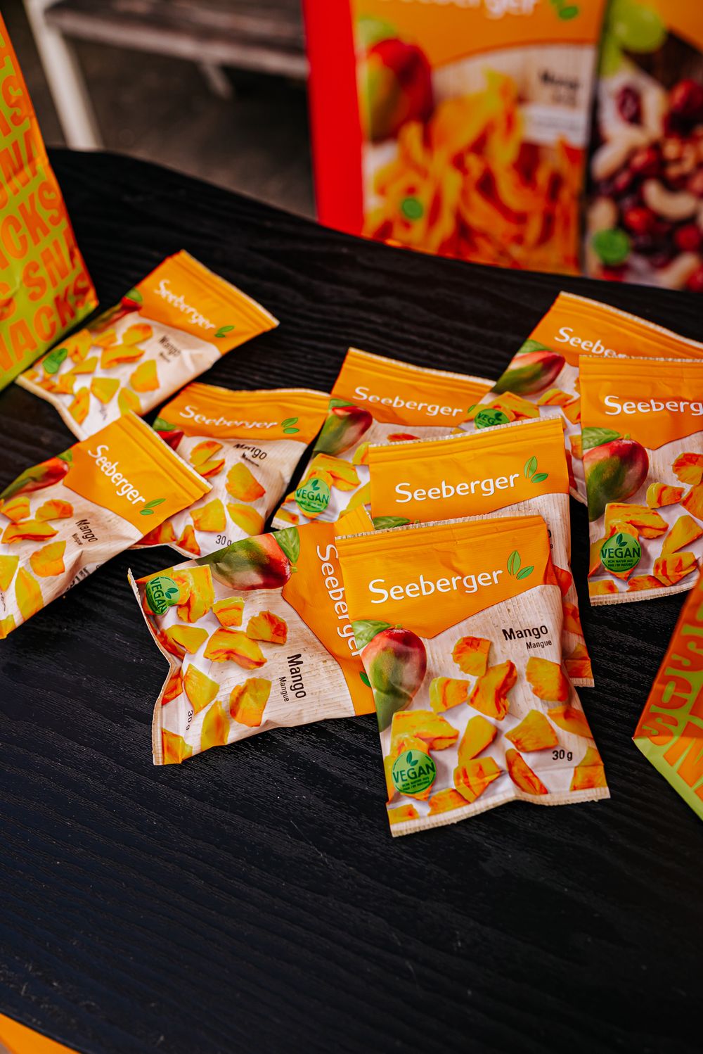 Multiple orange Seeberger brand snack packets scattered on a dark wooden surface in a diagonal line.