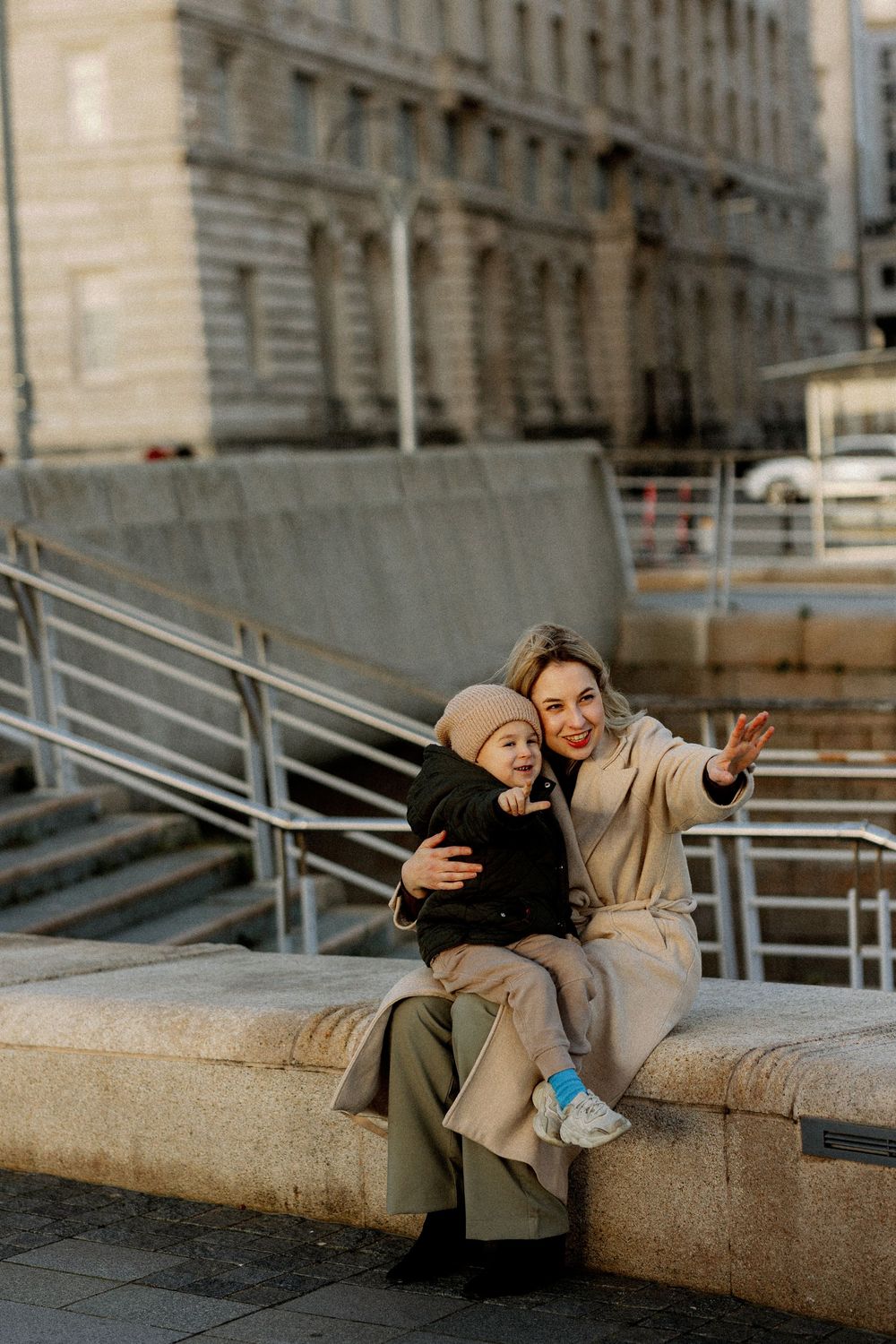 A sequence of four photos showing a couple in beige coats playfully posing on stone steps in an urban setting.