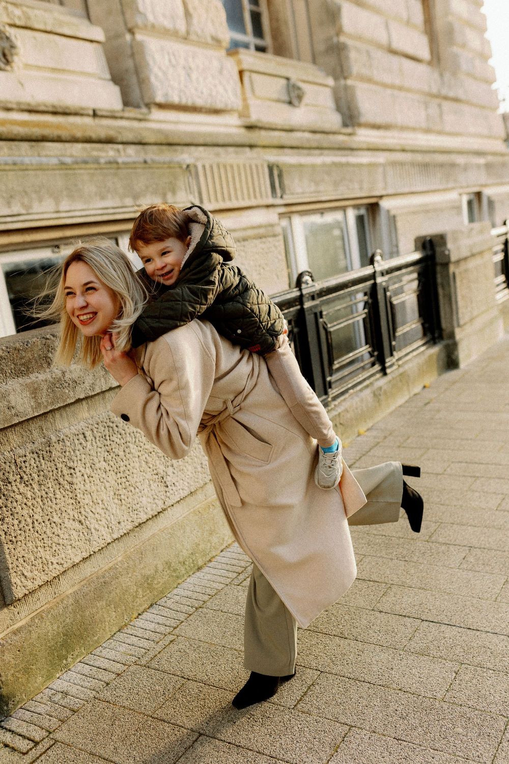 A sequence of playful poses showing someone in a beige coat leaning against a stone wall outdoors.