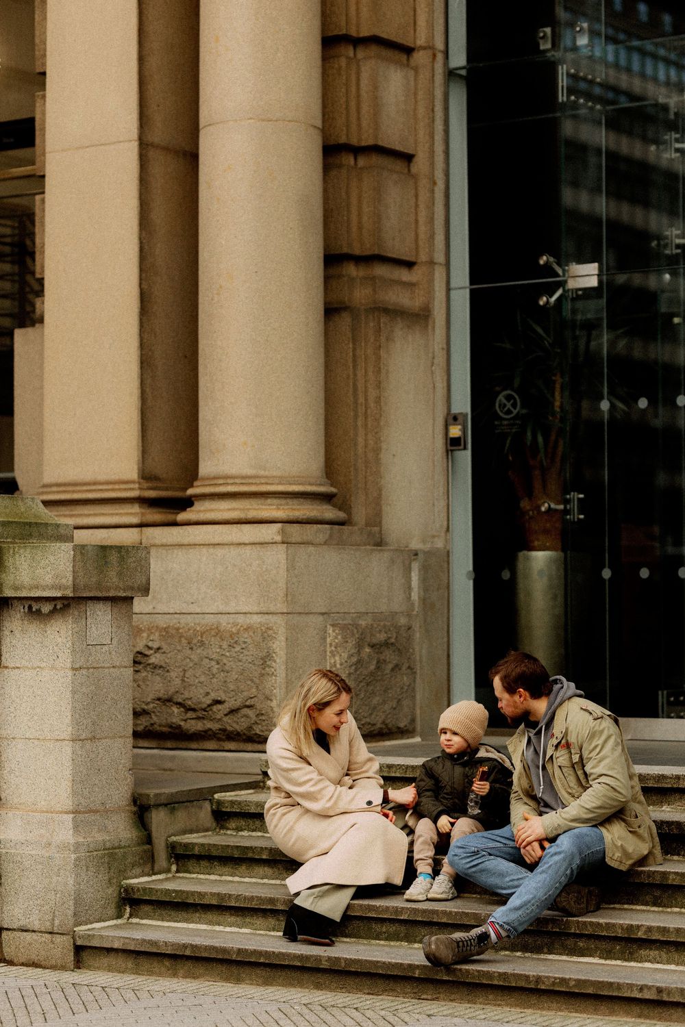 A group of people sit and chat on stone steps outside a building with classical columns.