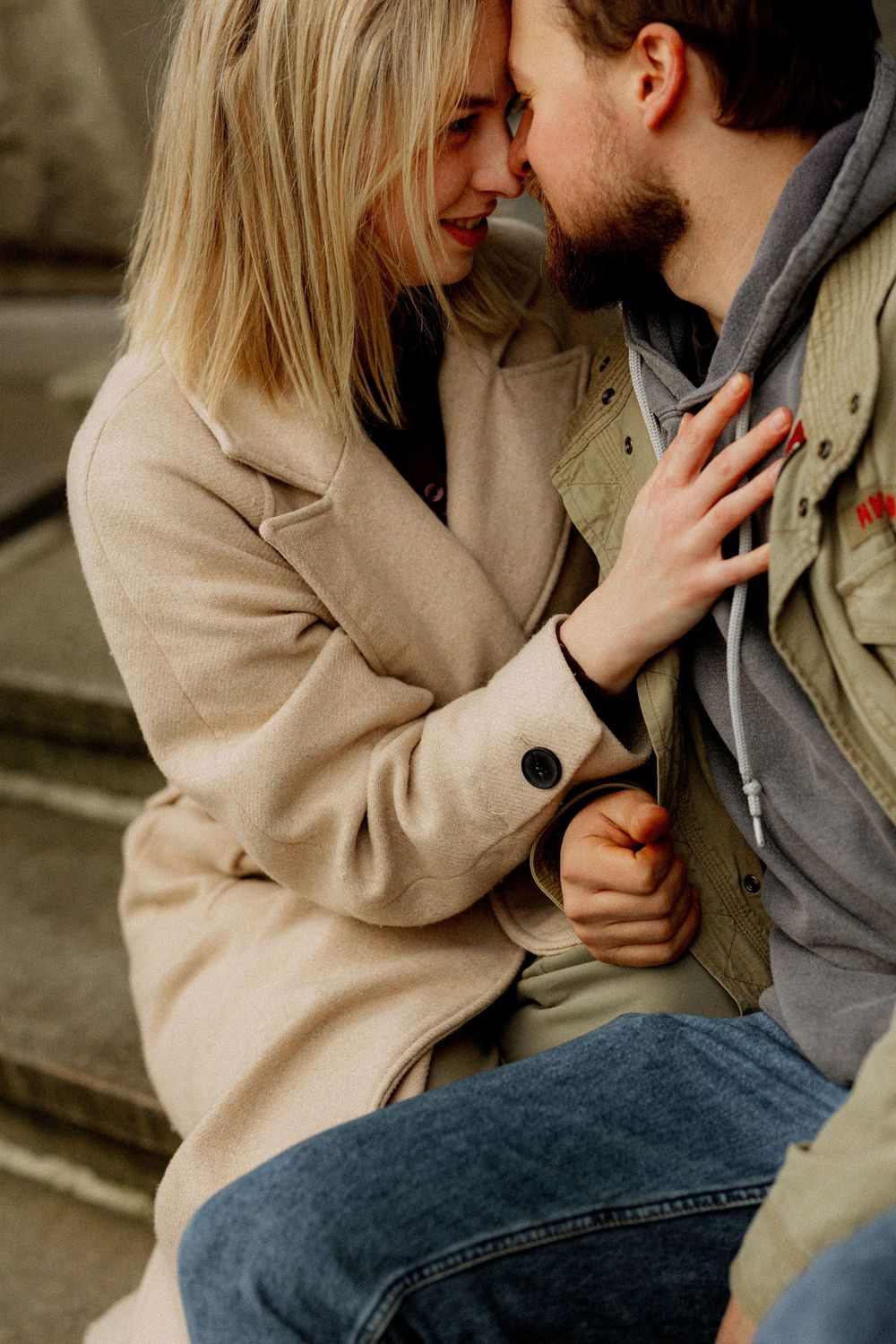 A romantic couple in casual winter wear share an intimate moment on stone steps outdoors.