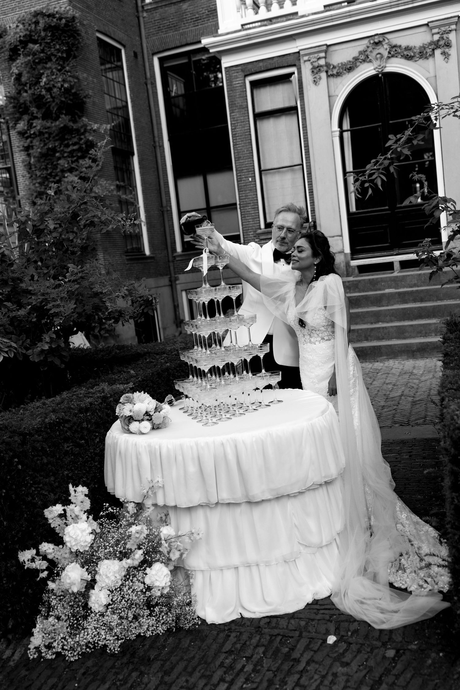 Black and white photo of newlyweds dancing near elegant reception tables with champagne towers.