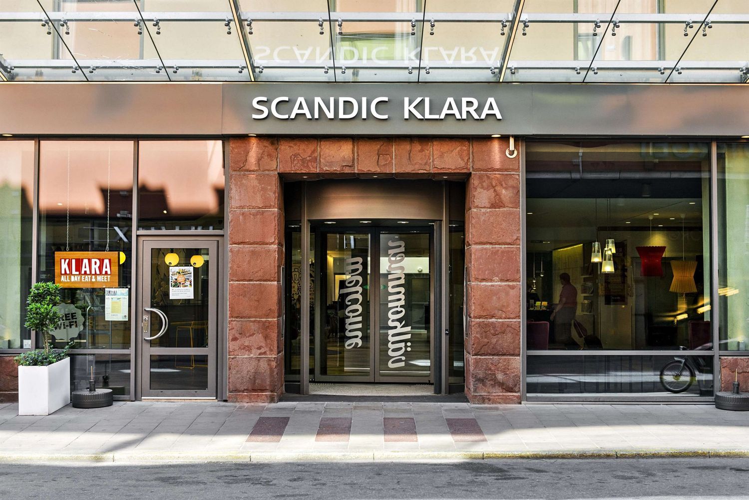 Modern hotel exterior with glass windows and signage reading Scandic Klara along a city street.