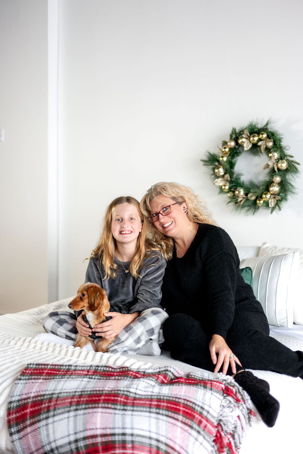 Mother and daughter smiling together with dachshund dog on bed with Christmas holiday wreath.