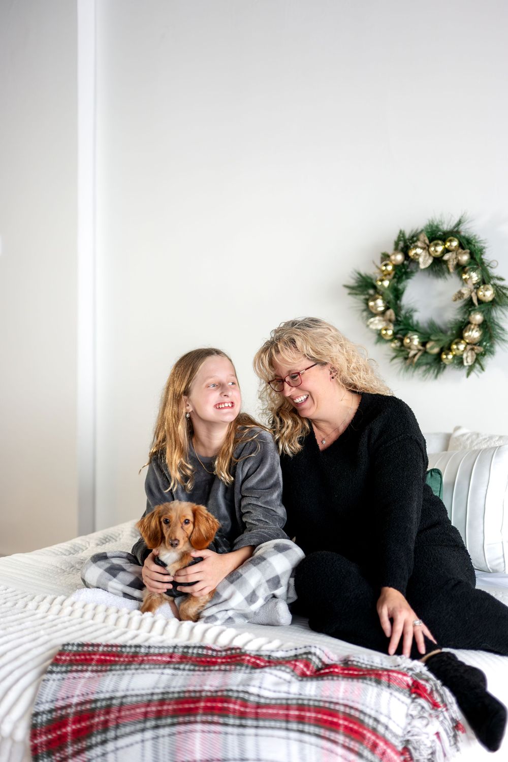 Mother and daughter laughing together with dachshund dog on bed decorated for Christmas.