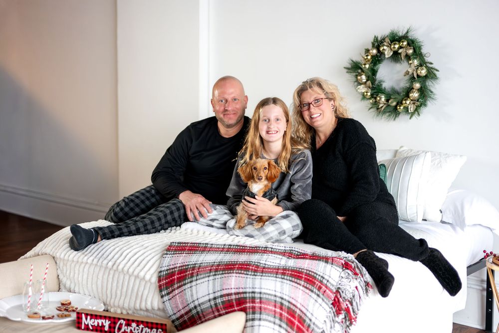 Parents and daughter with dachshund puppy sitting together on bed with Christmas decorations.