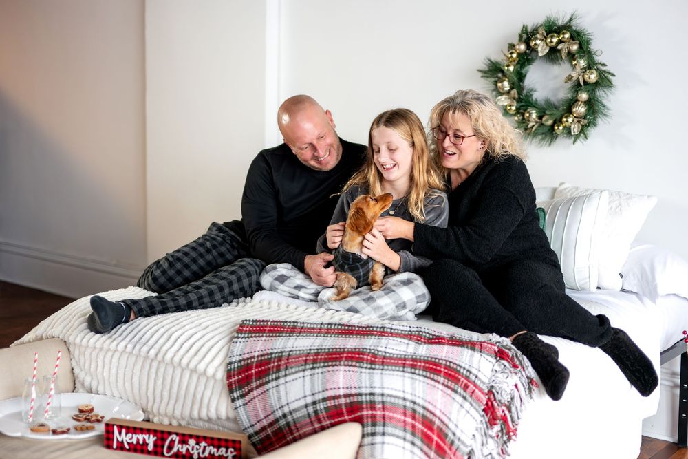 Happy family laughing together with dachshund dog on bed with Merry Christmas sign and wreath.