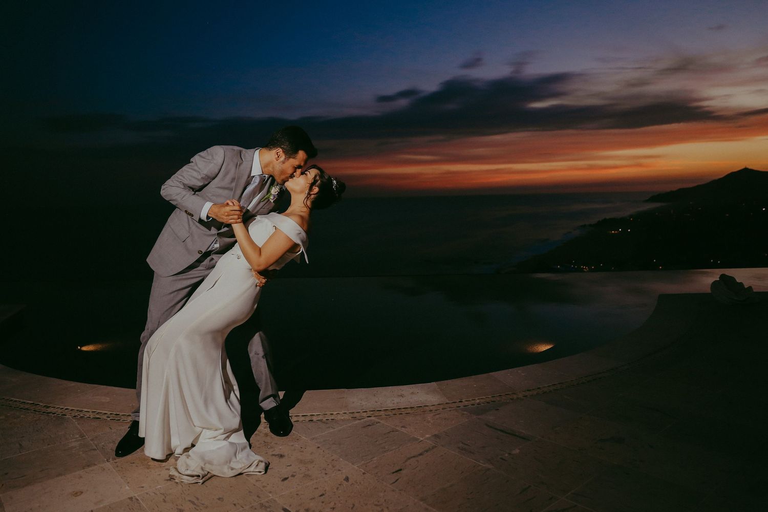 A couple stands silhouetted against a vibrant desert sunset sky in a romantic wedding photo. Pedregal Los Cabos Wedding Photographer