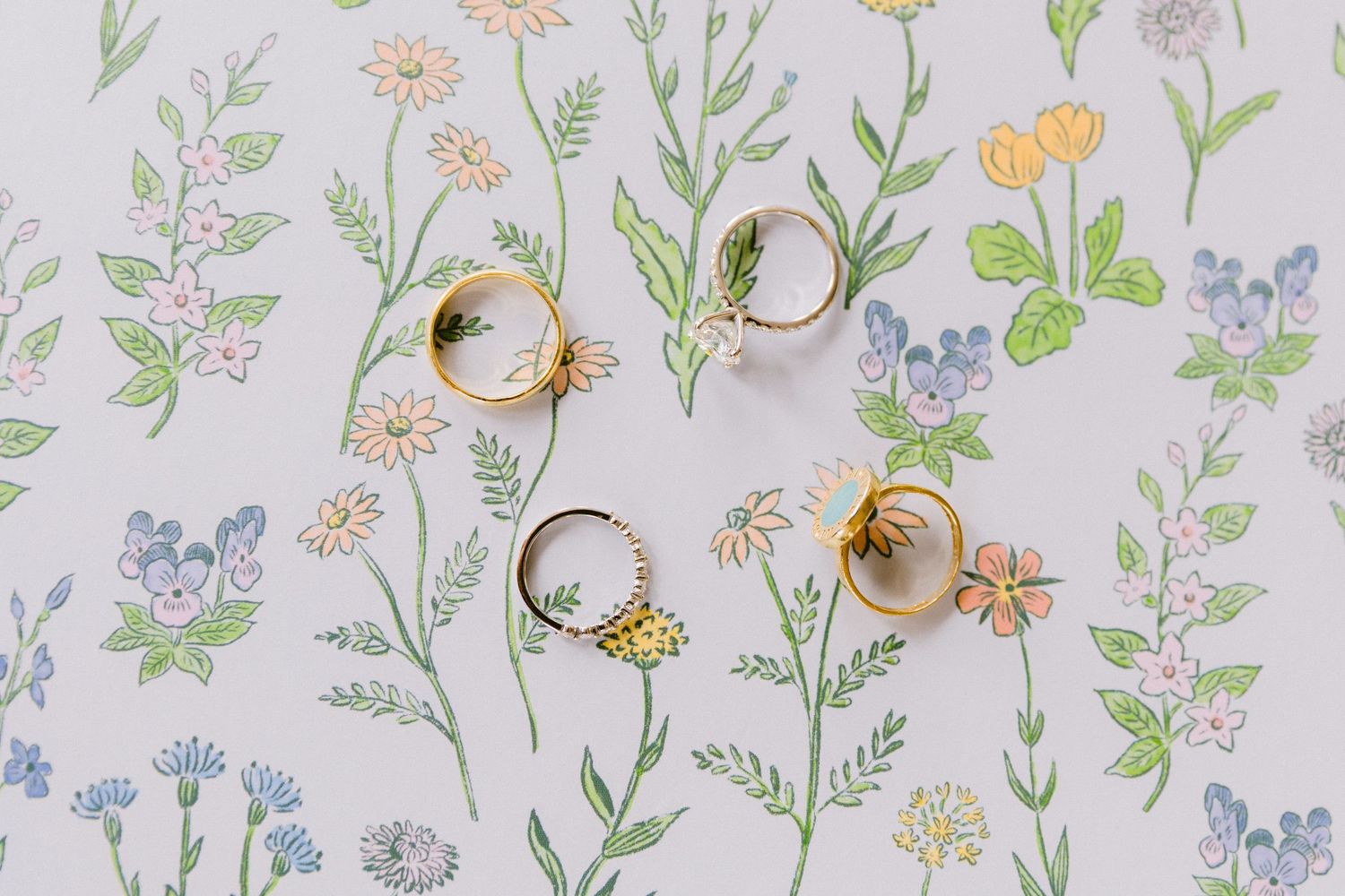 Delicate floral wallpaper pattern with yellow daisies, blue forget-me-nots, and green leaves on a pale background.