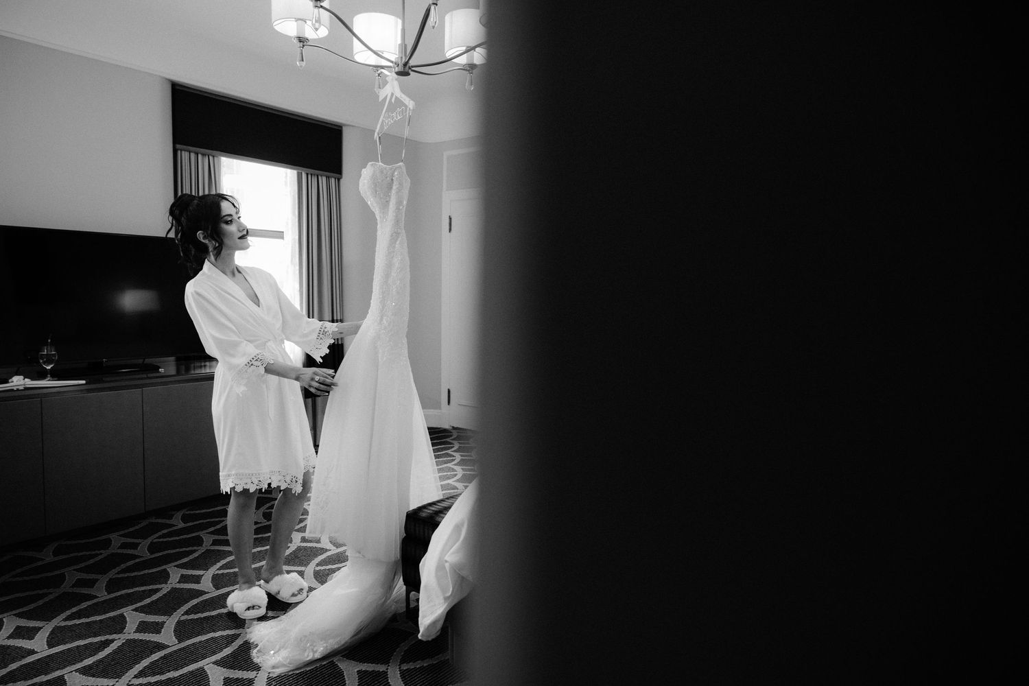 Black and white wedding photography captures intimate moments of a bride getting ready in a sunlit room.