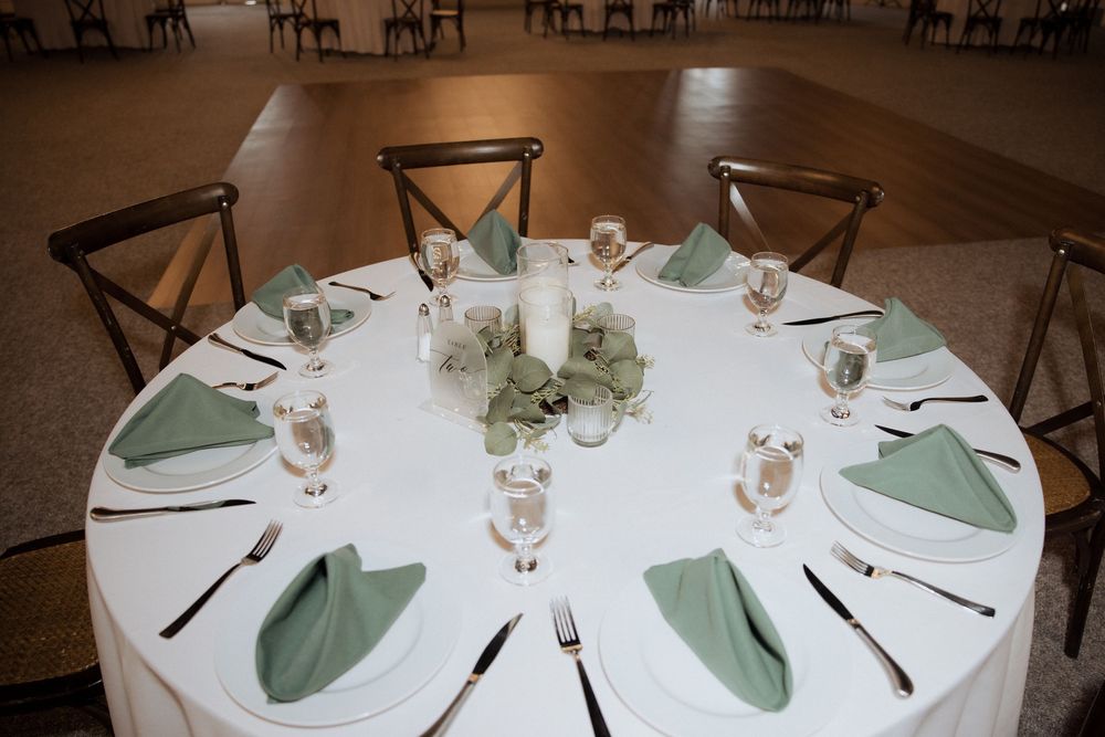 Elegant round banquet tables with white linens, mint green napkins and formal place settings arranged in a reception venue.